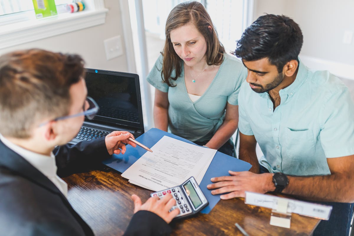 Property agent with calculator discussing documents and pricing with a couple across an office table