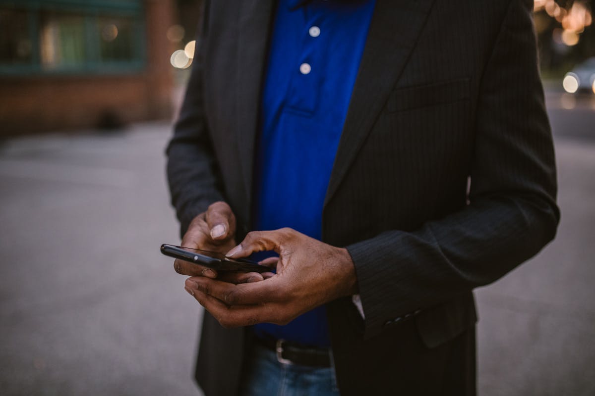 Business professional in a dark blazer using a smartphone outdoors, representing a Singapore property agent sending a follow-up message between viewings