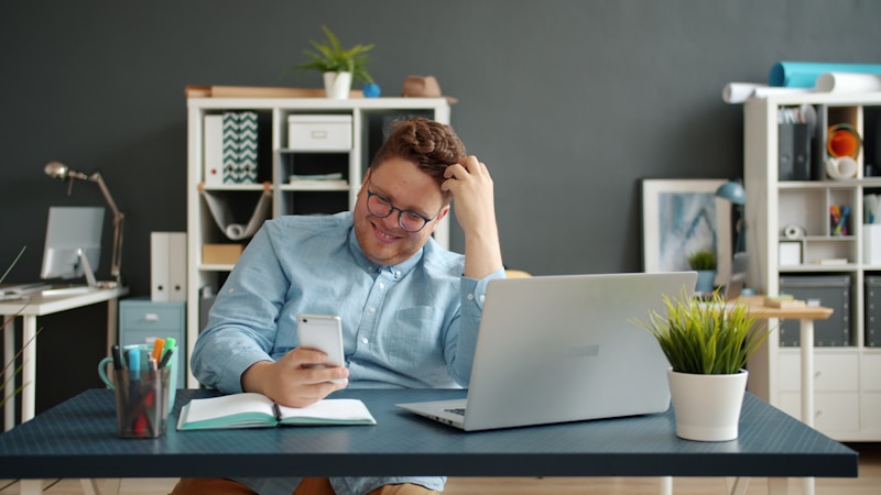 Professional at an organized desk checking their smartphone with laptop open, representing a property agent building a personal productivity system