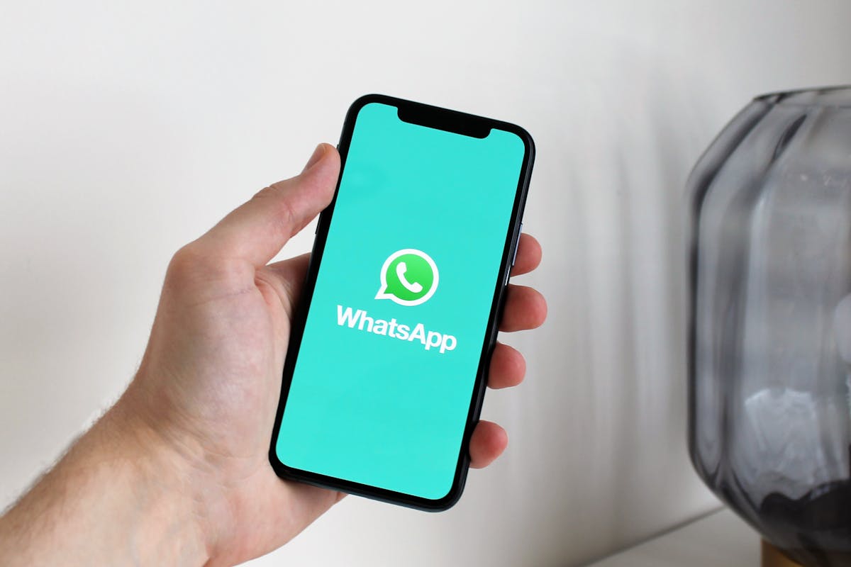 Hand holding a smartphone displaying the WhatsApp app splash screen, representing a Singapore property agent's WhatsApp client list